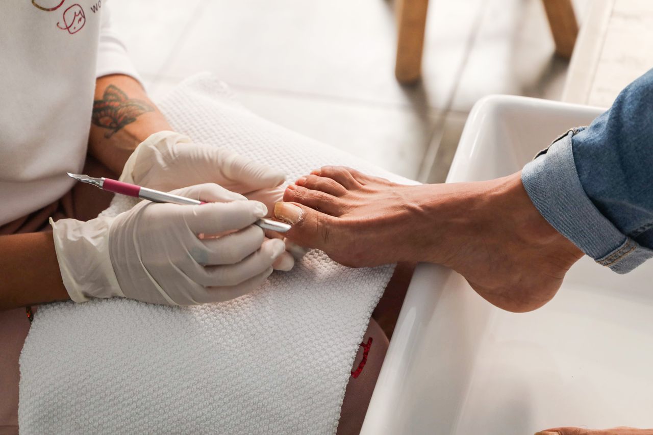 Pedicure session showing gloved hands performing nail care on foot.