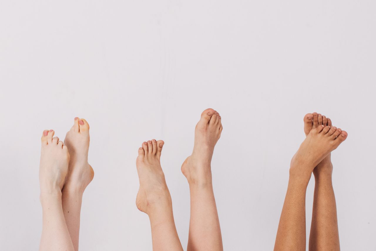 Four pairs of diverse feet raised against a plain white backdrop, capturing unity and diversity.